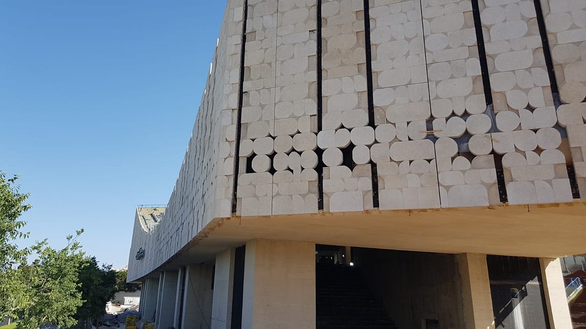 הספרייה הלאומית בירושלים בזמן הבנייה: נפח חזית עליון בגוון בהיר, נשען על עמודי בטון לבן חשוף בטקסטורת לוחות עץ